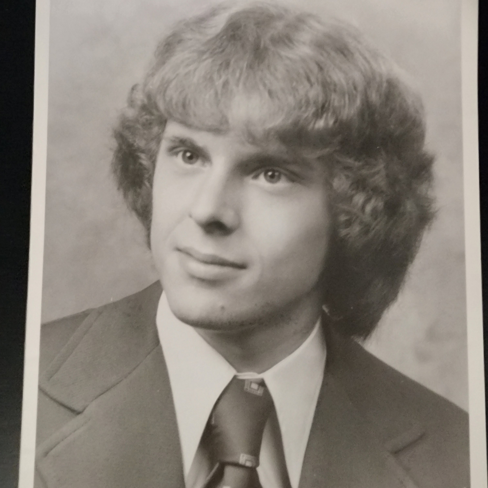 Black-and-white portrait of a young man in a suit and tie with a soft smile.