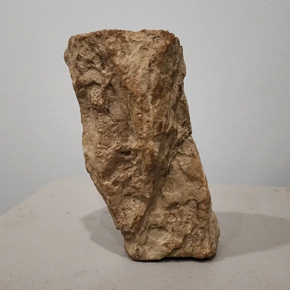 Rugged beige rock standing upright on a light gray tabletop, with a plain gray wall in the background.